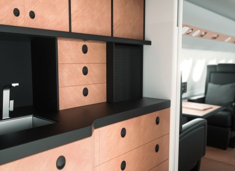 Flugzeugküche mit Natursteinfurnier Elegante Bordküche in einem Privatjet mit Schubladenfronten aus warmem Natursteinfurnier und schwarzer Arbeitsfläche.