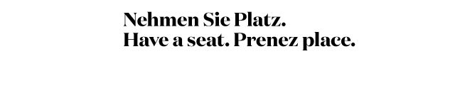 Mehrsprachiger Schriftzug: "Nehmen Sie Platz" Schriftzug "Nehmen Sie Platz. Have a seat. Prenez place." in drei Sprachen auf weißem Hintergrund.