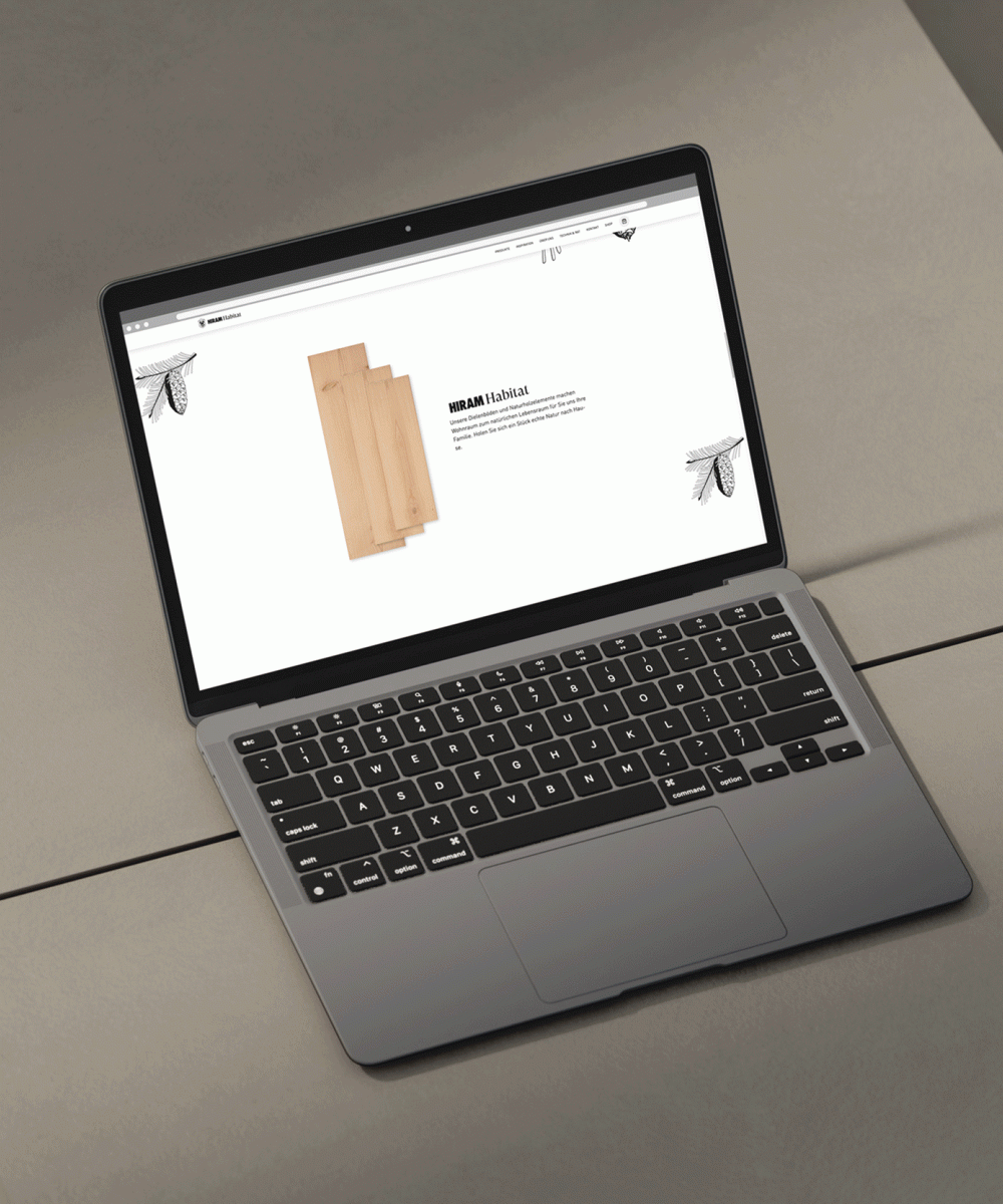 Laptop auf grauem Tisch zeigt Webseite von HIRAM Habitat mit Darstellung von Holzpaneelen