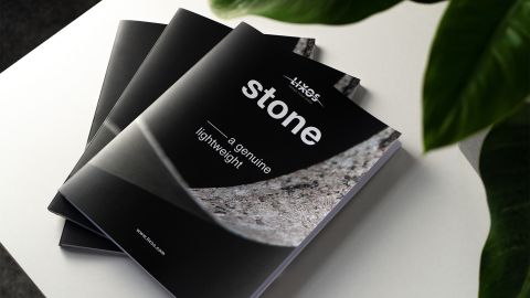 LIXOS Natursteinfurnier Katalog Drei schwarze LIXOS-Broschüren mit Natursteinfurnier-Cover und dem Titel „stone – a genuine lightweight“ auf weißem Tisch.